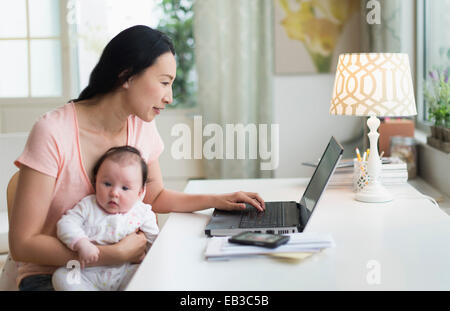 Asian mother with baby working from home Stock Photo