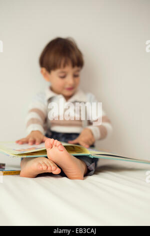 Boy sitting on his bed reading a book Stock Photo
