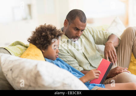 Father and son reading book in living room Stock Photo