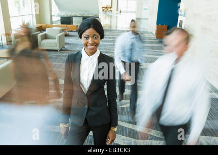 Businesswoman standing still in busy office lobby Stock Photo