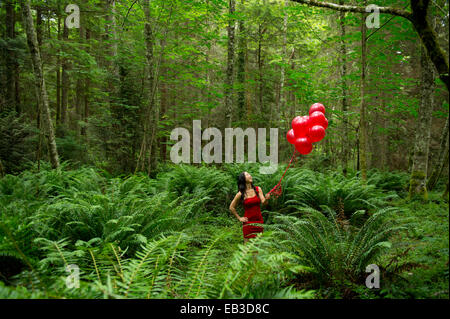 Korean woman holding red balloons in lush forest Stock Photo