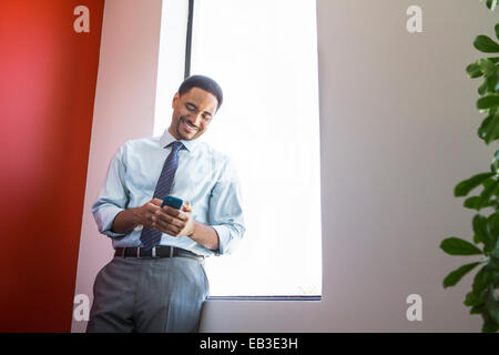 Black businessman using cell phone at office window Stock Photo