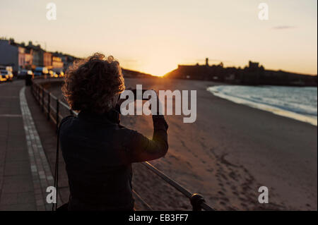 Woman taking iphone photo of sunset and castle Stock Photo