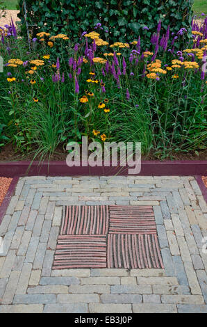 A close up garden view with a decorative mosaic stone insert in by a border of Achellia, Verbena and Veronica Stock Photo