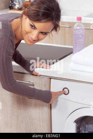 smiling woman pressing a button on her washing machine Stock Photo