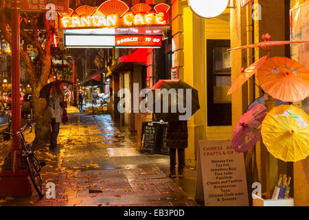 Chinese couple at Fan Tan alley entrance in Chinatown on rainy night-Victoria, British Columbia, Canada. Stock Photo