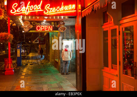 Young man reading menu outside Chinese restaurant in Chinatown on rainy  night-Victoria, British Columbia, Canada. Stock Photo