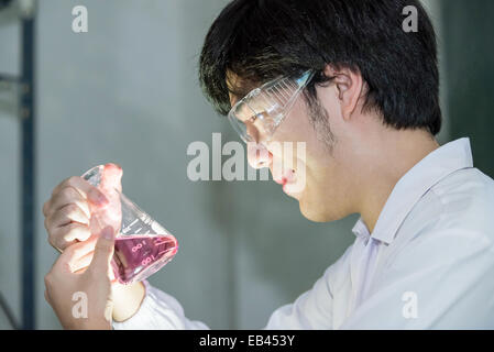 Asian scientist in white uniform looking at a test beaker in laboratory Stock Photo