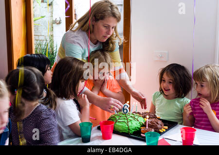 A boy blowing out the candles on his cake at his birthday party surrounded by his friends. Stock Photo