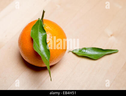 mandarin with two green leaves on a light wooden table Stock Photo