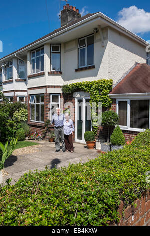 Pensioner couple standing in front of well kept semi-detached suburban house in Cardiff, the capital city of Wales. Stock Photo