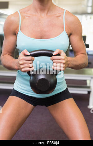 Mid section of a woman lifting kettle bell in gym Stock Photo