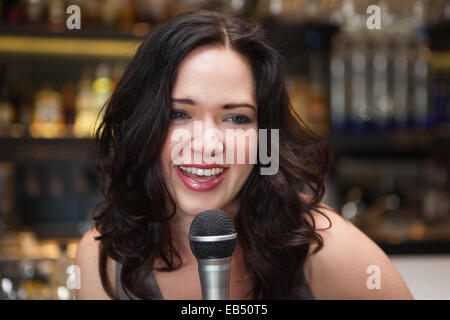 Happy brunette singing into mic Stock Photo