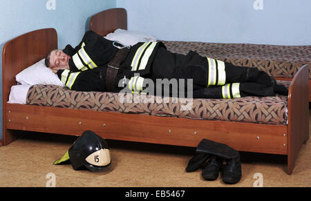 Firefighter sleeping dressed in Bunker gear on the bed Stock Photo