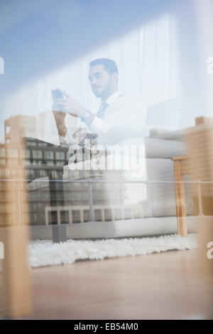 Businessman texting on his couch seen through glass Stock Photo