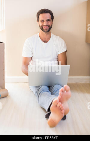 Happy man using laptop surrounded by boxes Stock Photo
