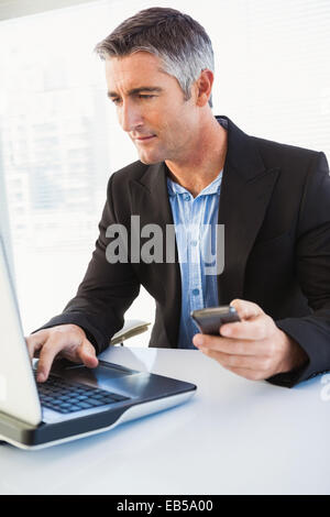Businessman using laptop and holding smartphone Stock Photo