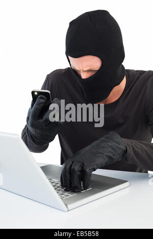 Hacker using laptop and phone Stock Photo