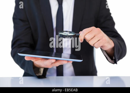Businessman looking at his tablet through magnifying glass Stock Photo