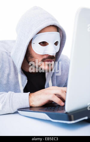Man wearing mask while hacking into laptop Stock Photo