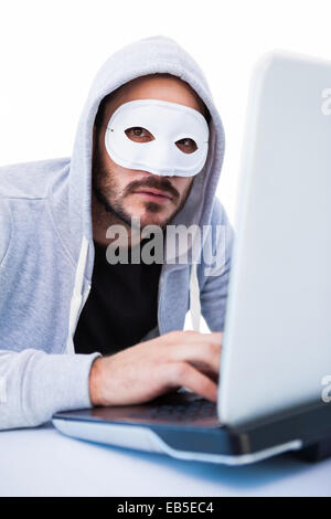 Man wearing mask while hacking into laptop Stock Photo