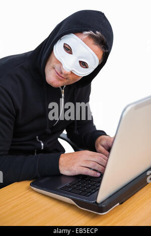 Hacker with white mask using laptop and looking at camera Stock Photo