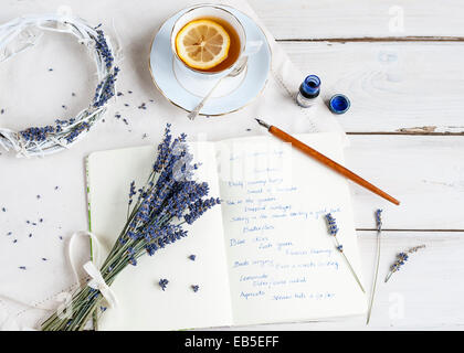 Overhead shot of a bunch of lavender on a notebook, with handwriting, on white table, with pen, ink, wreath and teacup Stock Photo