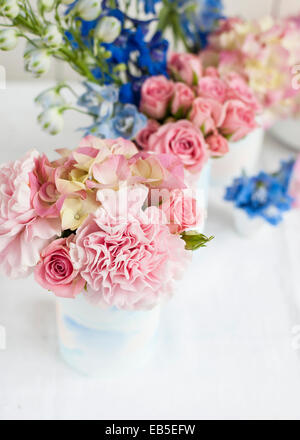 blue delphinium, pink roses, hydrangeas, carnation in tins decorated with painted watercolour paper - white backdrop Stock Photo