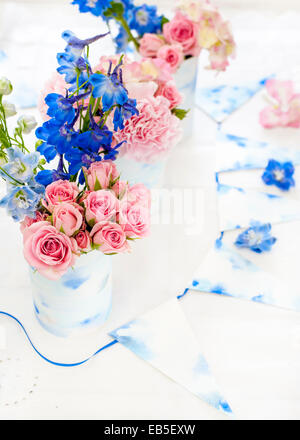 blue delphinium, pink roses, hydrangeas, carnation in tins decorated with painted watercolour paper and white and blue bunting Stock Photo