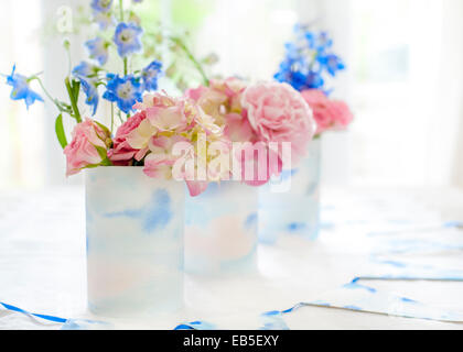 blue delphinium, pink roses, hydrangeas, carnation in tins decorated with painted watercolour paper and white and blue bunting Stock Photo