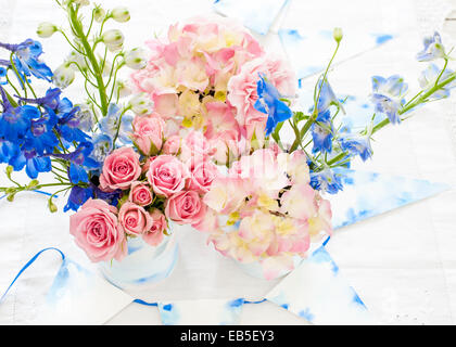 blue delphinium, pink roses, hydrangeas, carnation in tins decorated with painted watercolour paper and white and blue bunting Stock Photo