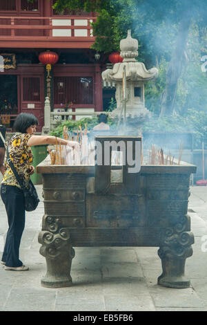 one woman placing pray sticks into ornamental earn at a Chinese shrine Stock Photo
