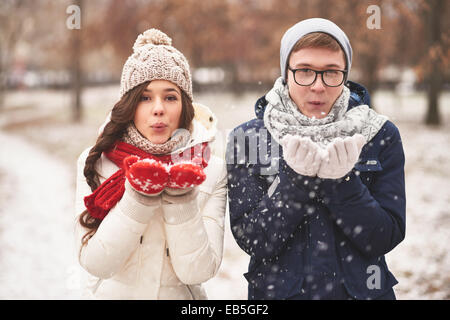 Portrait of cute young dates in casual winterwear blowing snowflakes from palms Stock Photo