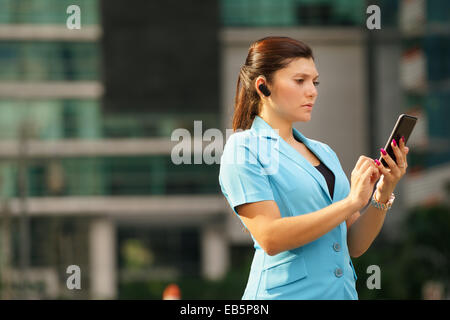Adult hispanic person with mobile phone and wireless bluetooth headset, talking on telephone in the street out office buildings Stock Photo