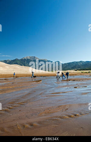 Family crossing Medano Creek, dunes and Sangre de Cristo Mountains, Great Sand Dunes National Park and Preserve, Colorado USA Stock Photo