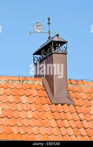 decorative ornamental chimney smokestack on tile roof with metal weathercock Stock Photo