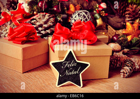 a star-shaped chalkboard with the text feliz natal, merry christmas in portuguese, on a rustic wooden table full of gifts and ch Stock Photo