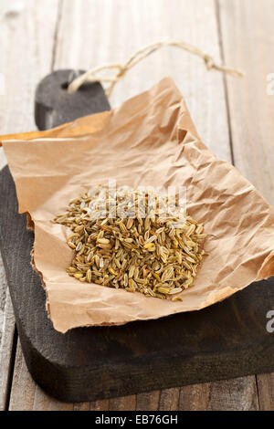 Heap of dried organic fennel seeds on wooden board on kitchen table Stock Photo