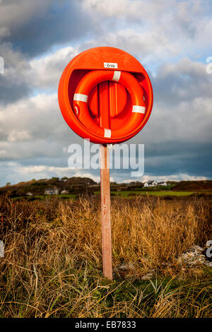 Lifebelt on a stand in grass at the edge of the beach at Rhoscolyn, Anglesey, Wales, GB on a sunny evening Stock Photo