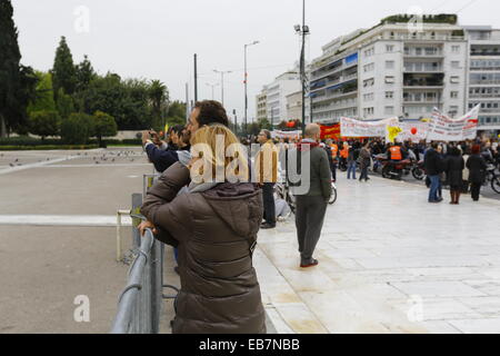 Athens, Greece. 27th November 2014. Tourists watching the changing of the Guards, while the protest march passes by the greek Parliament. Tens of thousands Greeks followed the call by Greek Trade Union for a one day general strike and protest march to the Greek parliament. They protested against the austerity measures by the Greek government. Credit:  Michael Debets/Alamy Live News Stock Photo