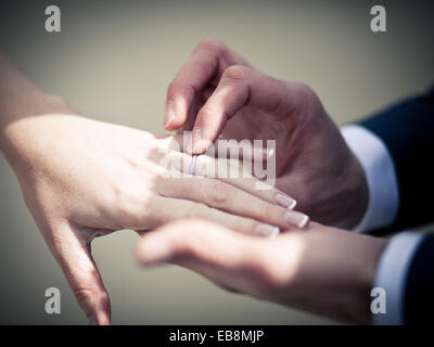 groom placing a wedding ring on a brides hand in summer sunlight out door wedding, exchanging of rings at the ceremony Stock Photo