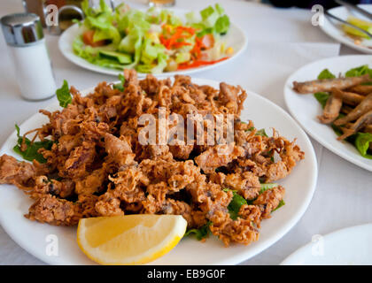 Spanish tapa of deep fried tiny squid, chopitos, garnished with a lemon slice.  Salad and fried sardines in the background. Stock Photo
