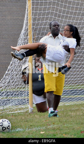 Coach carries injured soccer player off the field during a high school game Stock Photo