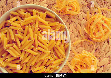 a bowl with uncooked penne rigate and some uncooked tagliatelle, with its characteristic nest shape Stock Photo