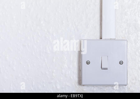 Light switch mounted on white wall with copy space. Old square box style switch on wood-chip wall paper background. Stock Photo