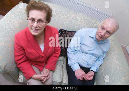 Older couple sitting on a sofa at home smiling, Stock Photo