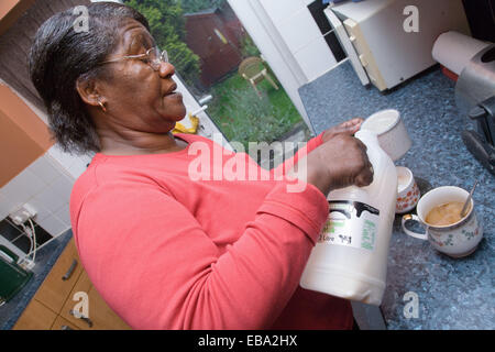 Older woman in her kitchen pouring milk into a cup of coffee, Stock Photo