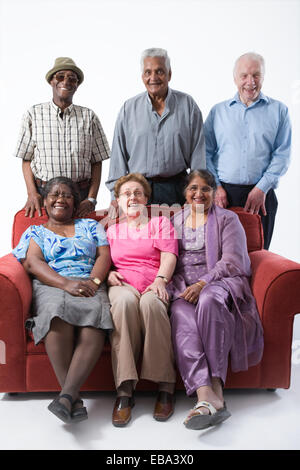 Multiracial group of older people sitting on a sofa together smiling, Stock Photo