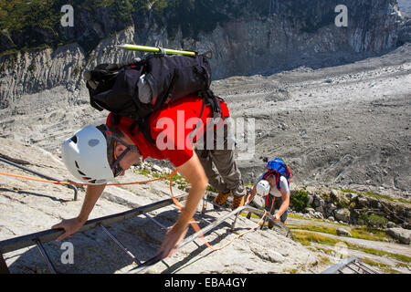 Climbers descend ladders leading down onto the Mer De Glace from near the Montenvers railway station. The railway was built in Victorian times to take tourists up to the glacier, it has subsequently thinned 150 meters since 1820, and retreated by 2300 Metres. In order to access the glacier you now have to climb down over 100 metres on ladders. Stock Photo