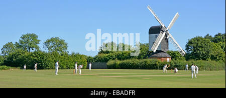 Iconic quintessential England idyllic village green cricket match bowler batsman & fielders Mountnessing Post Mill beyond in Essex countryside UK Stock Photo